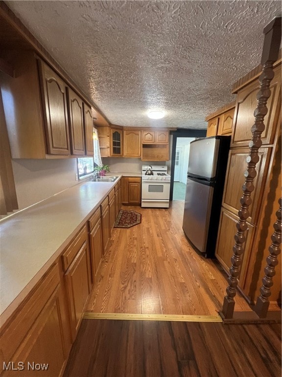 kitchen with light wood-type flooring, a textured ceiling, stainless steel refrigerator, and white gas range oven