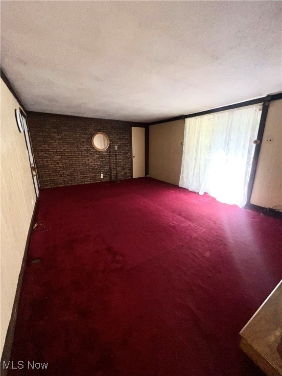 carpeted spare room featuring a textured ceiling and brick wall