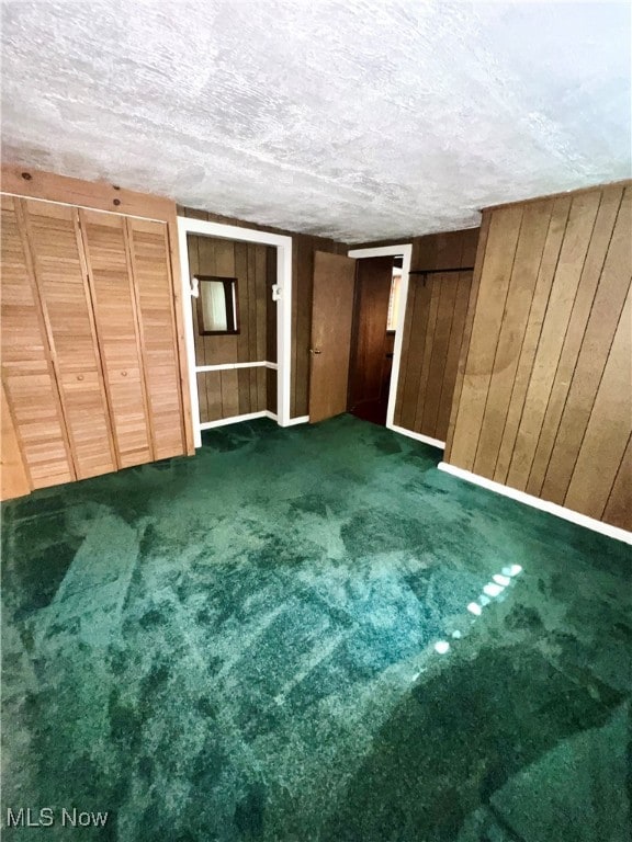 unfurnished bedroom featuring dark carpet, wooden walls, and a textured ceiling