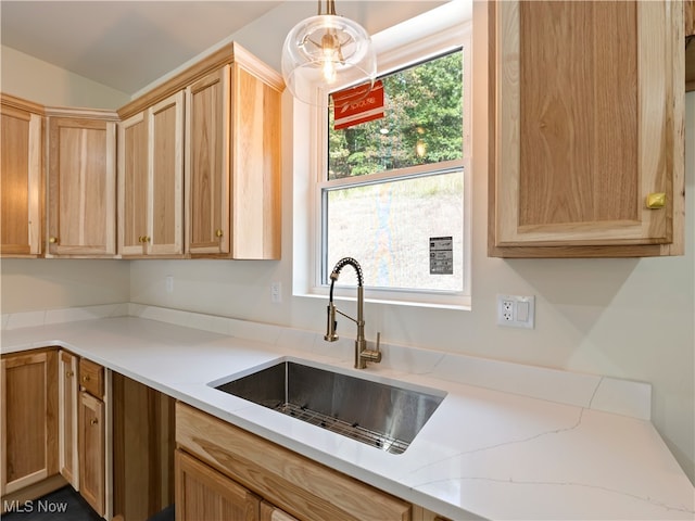 kitchen with light stone countertops, light brown cabinets, decorative light fixtures, and sink