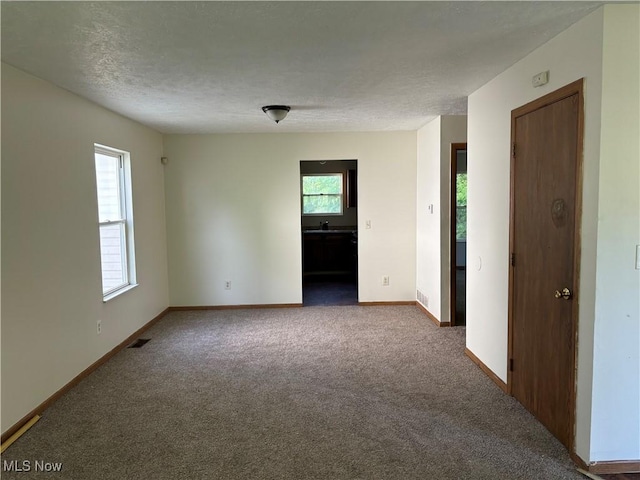 carpeted empty room featuring visible vents, baseboards, and a textured ceiling