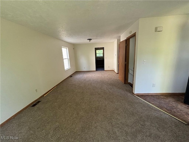 carpeted spare room with baseboards, visible vents, and a textured ceiling