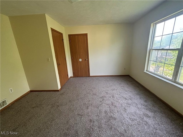 unfurnished room with carpet flooring, visible vents, a textured ceiling, and baseboards