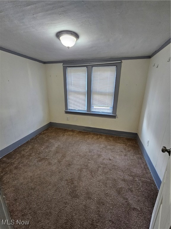 empty room featuring crown molding, dark carpet, a textured ceiling, and baseboards