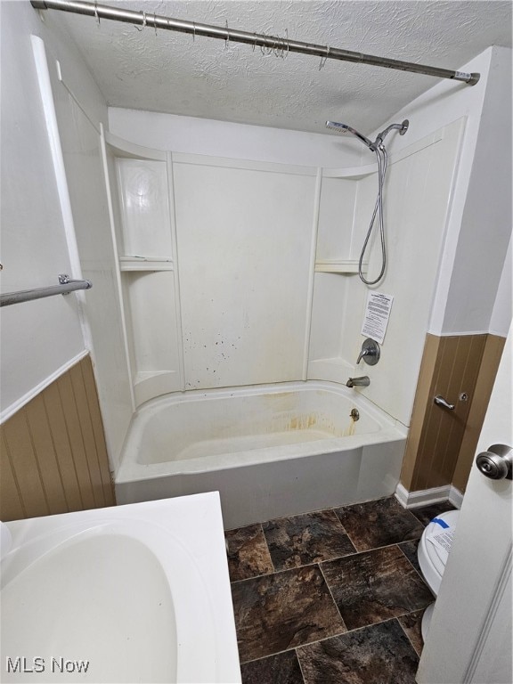 full bath featuring stone finish floor, a textured ceiling, toilet, and bathing tub / shower combination