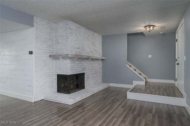 unfurnished living room with dark hardwood / wood-style flooring, a textured ceiling, and a brick fireplace