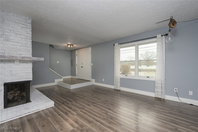 unfurnished living room featuring a textured ceiling, dark hardwood / wood-style floors, and a brick fireplace