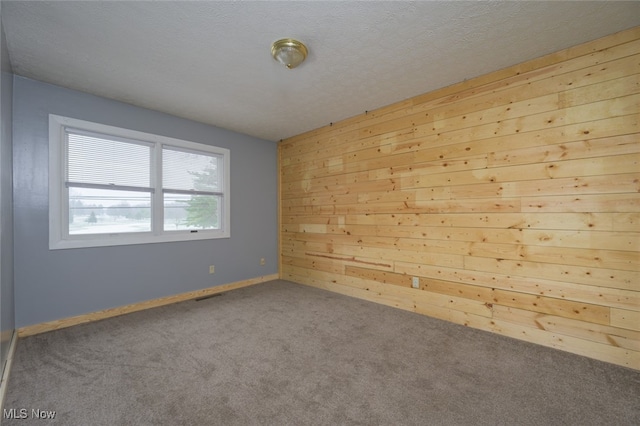 carpeted empty room with a textured ceiling and wooden walls