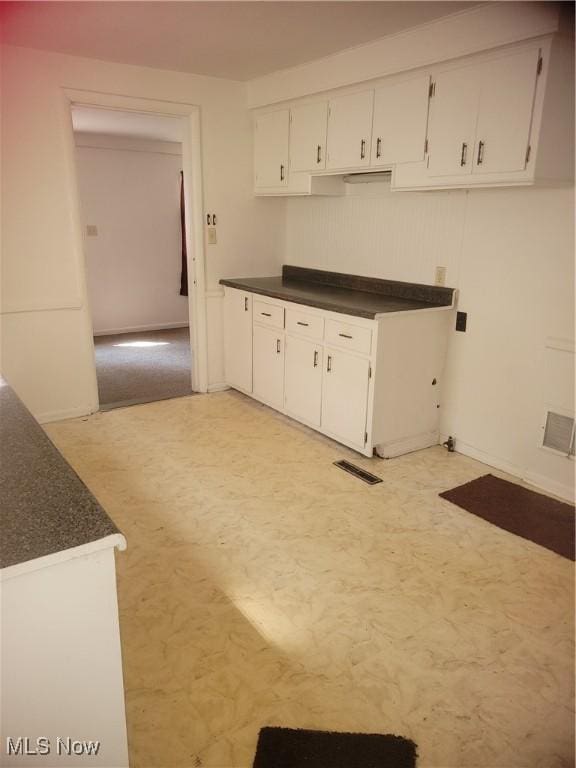 kitchen with dark countertops, visible vents, baseboards, light floors, and white cabinetry