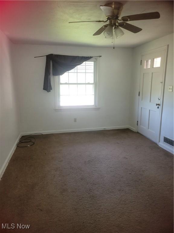 carpeted spare room with visible vents, baseboards, and ceiling fan