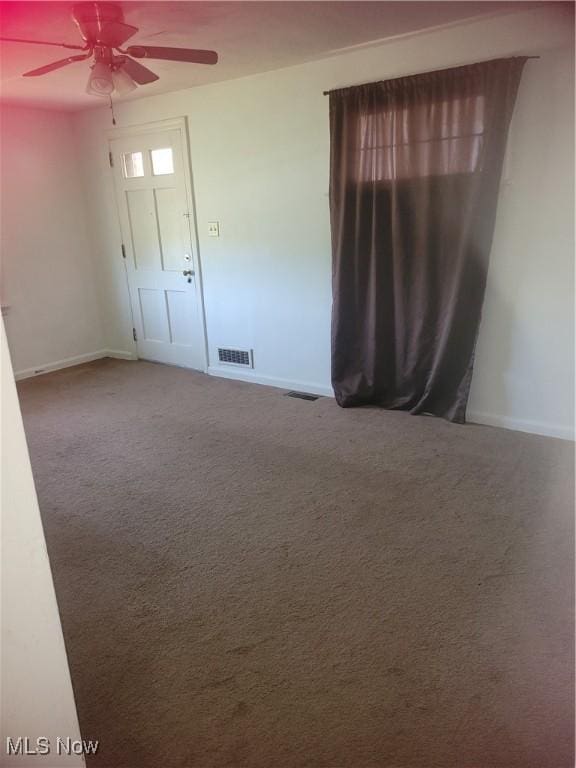 carpeted spare room with visible vents, baseboards, and a ceiling fan