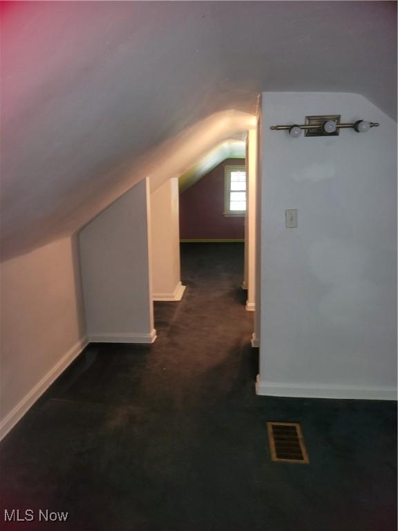 additional living space with visible vents, baseboards, carpet flooring, and vaulted ceiling