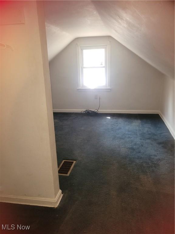 bonus room with dark carpet and vaulted ceiling