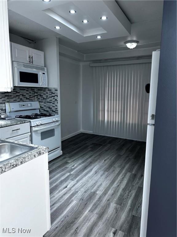 kitchen featuring white appliances, tasteful backsplash, wood finished floors, and white cabinetry