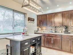 kitchen with a kitchen island, decorative backsplash, sink, hanging light fixtures, and dark brown cabinets