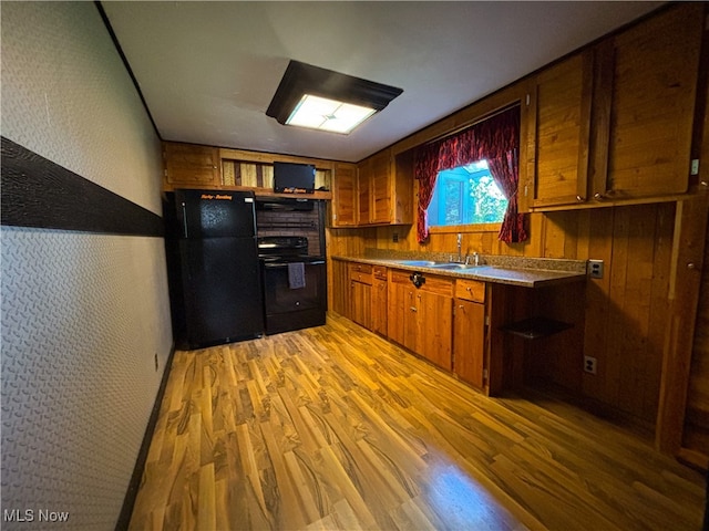 kitchen featuring sink, wooden walls, hardwood / wood-style floors, and black appliances