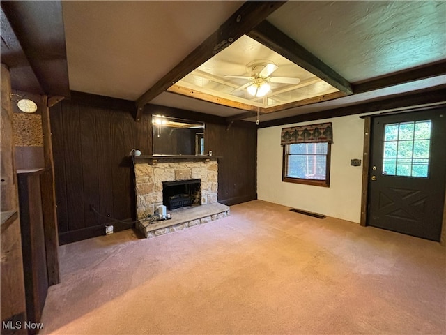 unfurnished living room with a fireplace, wood walls, beamed ceiling, ceiling fan, and carpet