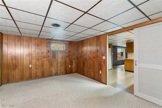 unfurnished room featuring a paneled ceiling, wood walls, and light carpet