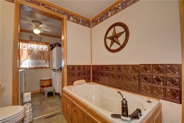 bathroom featuring a textured ceiling, ceiling fan, toilet, and a washtub