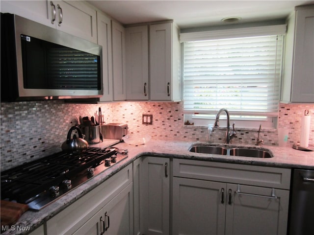 kitchen featuring light stone counters, backsplash, sink, and appliances with stainless steel finishes