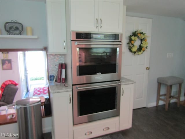 kitchen featuring double oven, white cabinetry, tasteful backsplash, light stone countertops, and dark hardwood / wood-style floors