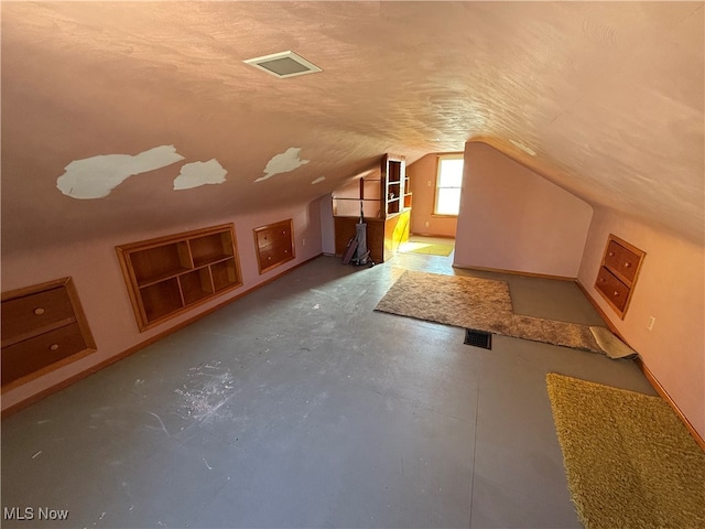 additional living space featuring a textured ceiling, concrete flooring, and vaulted ceiling