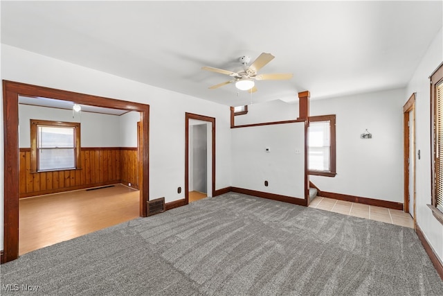 empty room featuring a wealth of natural light, light colored carpet, ceiling fan, and wooden walls