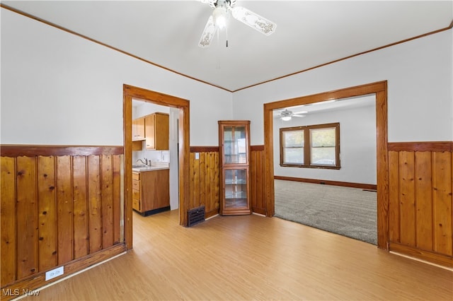 spare room featuring crown molding, ceiling fan, light wood-type flooring, and wooden walls