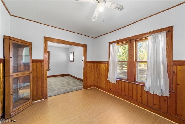 empty room featuring ornamental molding, ceiling fan, wood walls, and wood-type flooring