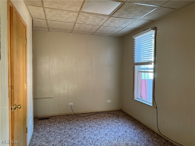 spare room featuring wooden walls, a drop ceiling, and carpet floors