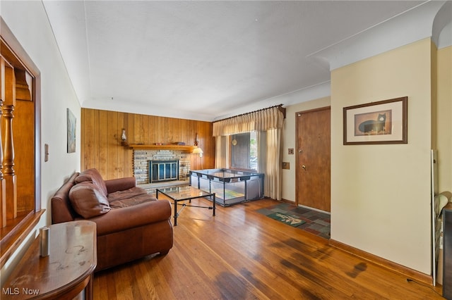 living room with wooden walls, dark hardwood / wood-style flooring, and a brick fireplace