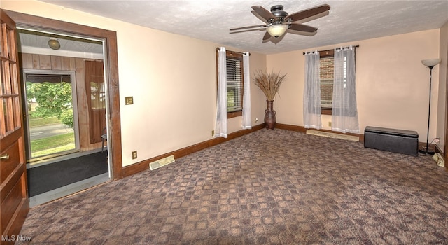 spare room featuring a textured ceiling, ceiling fan, dark colored carpet, and wooden walls