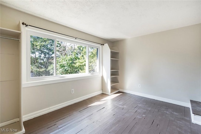 empty room with a textured ceiling, baseboards, and wood-type flooring