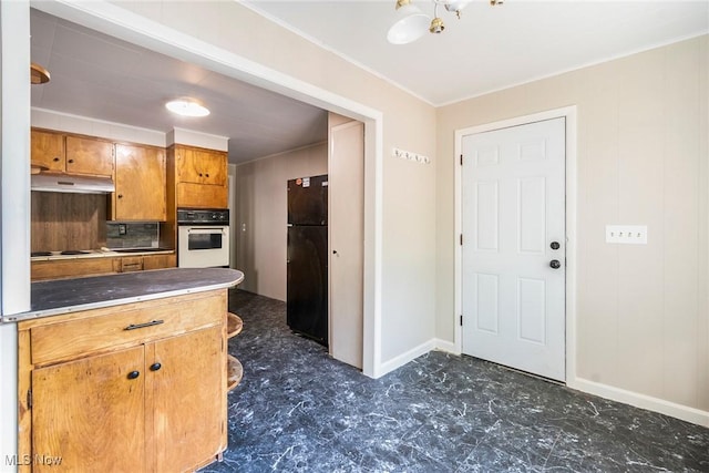 kitchen featuring cooktop, freestanding refrigerator, brown cabinets, under cabinet range hood, and oven