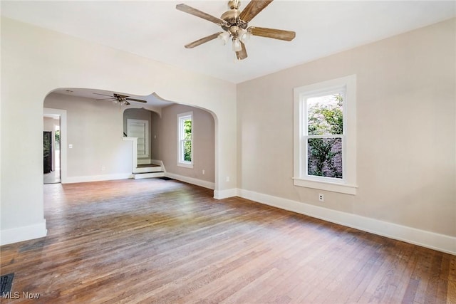 spare room featuring baseboards, ceiling fan, wood finished floors, stairway, and arched walkways