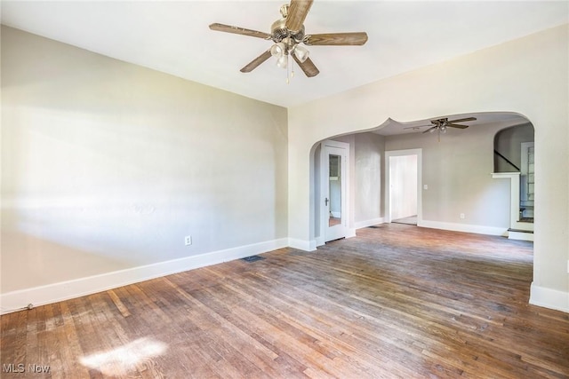 unfurnished room featuring wood finished floors, arched walkways, baseboards, and ceiling fan