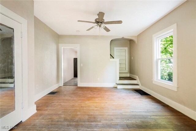 empty room featuring baseboards, arched walkways, visible vents, ceiling fan, and wood finished floors