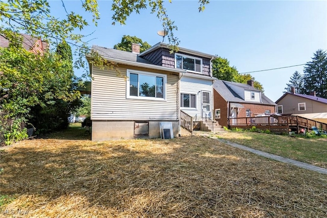 back of house featuring a chimney, entry steps, a deck, and a yard