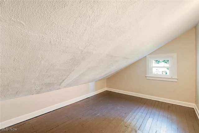 bonus room featuring dark wood-type flooring, baseboards, vaulted ceiling, and a textured ceiling