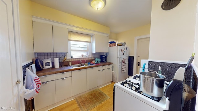 kitchen with white appliances, light hardwood / wood-style flooring, butcher block counters, tasteful backsplash, and sink