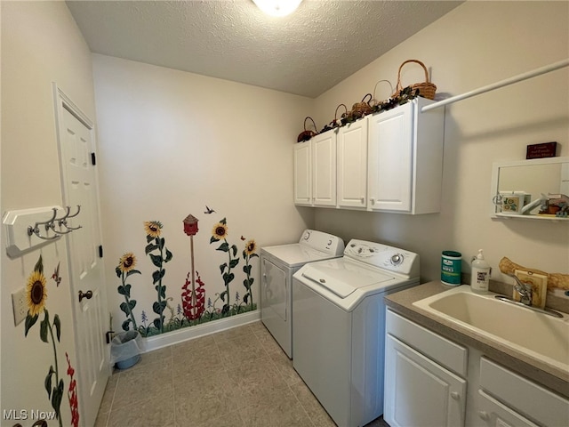 washroom featuring a textured ceiling, cabinets, washing machine and clothes dryer, and sink