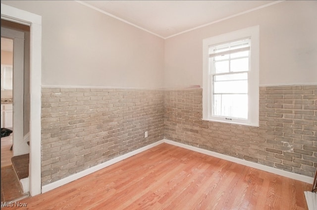 empty room with wood-type flooring, crown molding, and brick wall