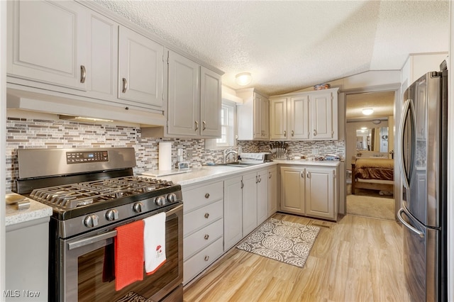 kitchen featuring vaulted ceiling, light wood-type flooring, stainless steel appliances, decorative backsplash, and a textured ceiling