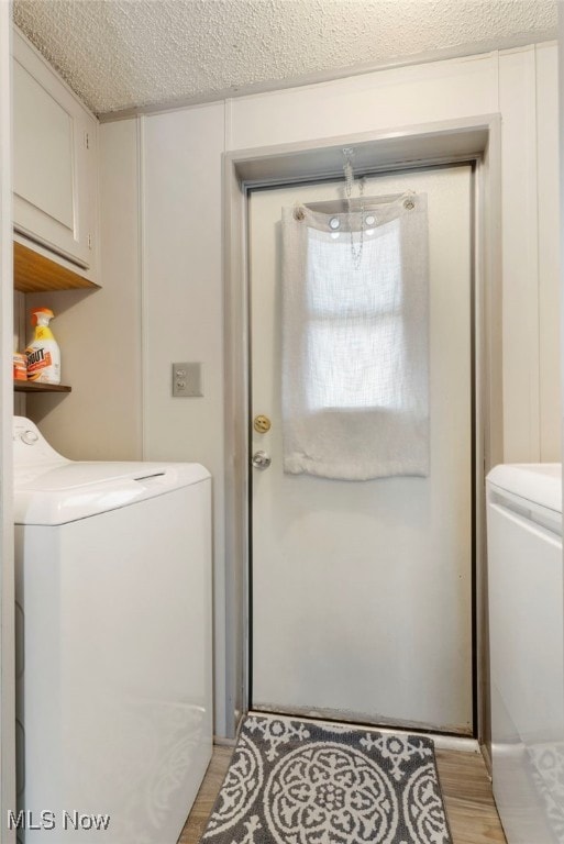 laundry room featuring light wood-type flooring, a textured ceiling, independent washer and dryer, and cabinets