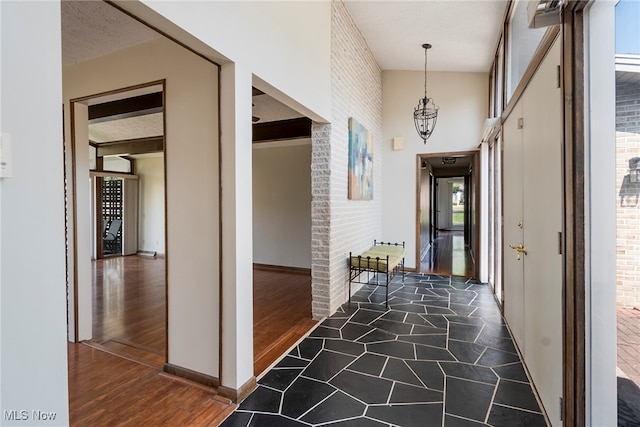 hall featuring a textured ceiling, brick wall, dark hardwood / wood-style floors, and an inviting chandelier