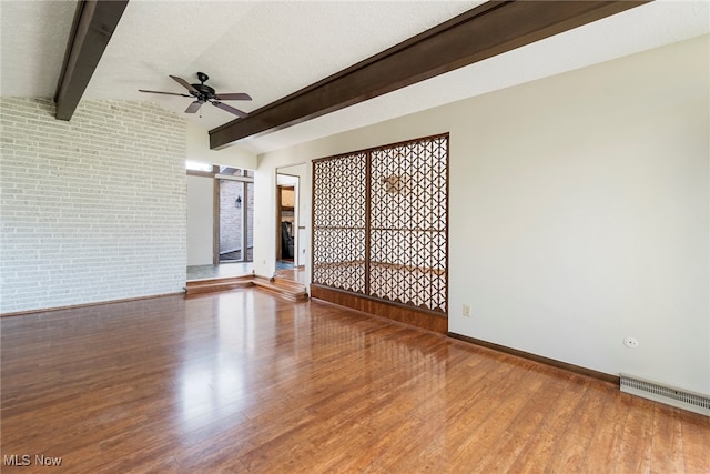 spare room with a textured ceiling, ceiling fan, vaulted ceiling with beams, hardwood / wood-style flooring, and brick wall