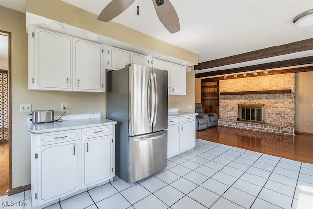 kitchen featuring white cabinets, a fireplace, light hardwood / wood-style flooring, stainless steel fridge, and ceiling fan