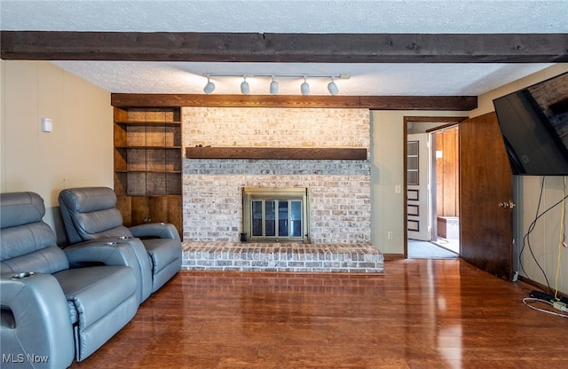 living room featuring beamed ceiling, a textured ceiling, rail lighting, wood-type flooring, and a brick fireplace