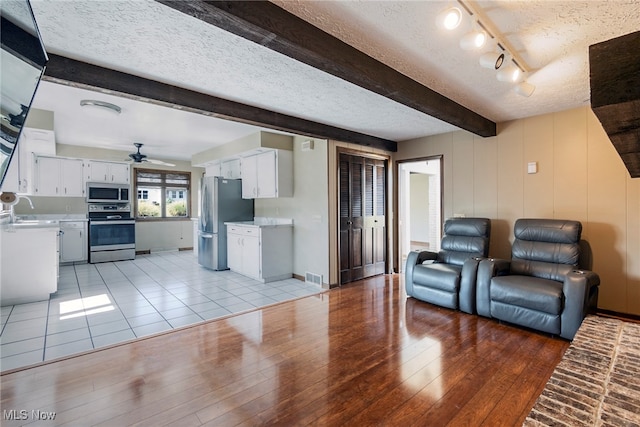 living room featuring light wood-type flooring, a textured ceiling, beam ceiling, and ceiling fan