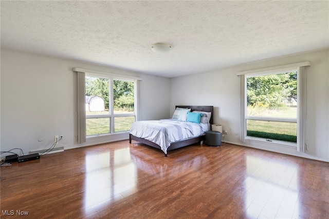 bedroom featuring a textured ceiling, dark hardwood / wood-style flooring, and multiple windows